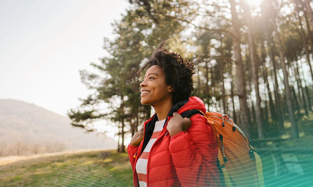 Photo of a young smiling woman carrying a backpack and hiking in the nature